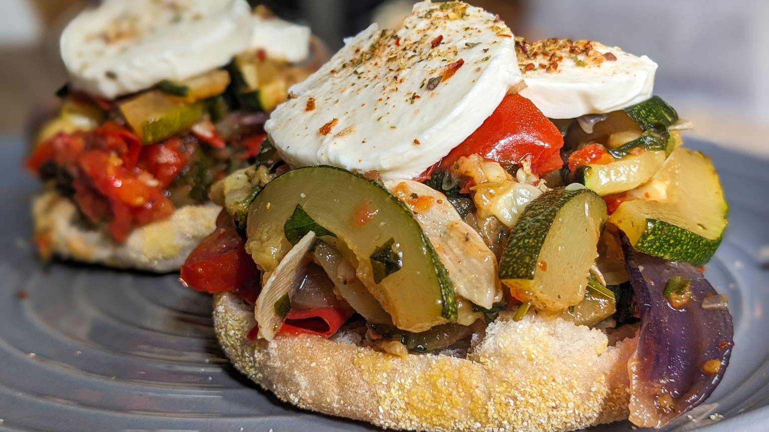 Auf einem Toastbrötchen liegt das angebratene Zucchini-Tomaten-Gemüse sowie Mozzarellascheiben.