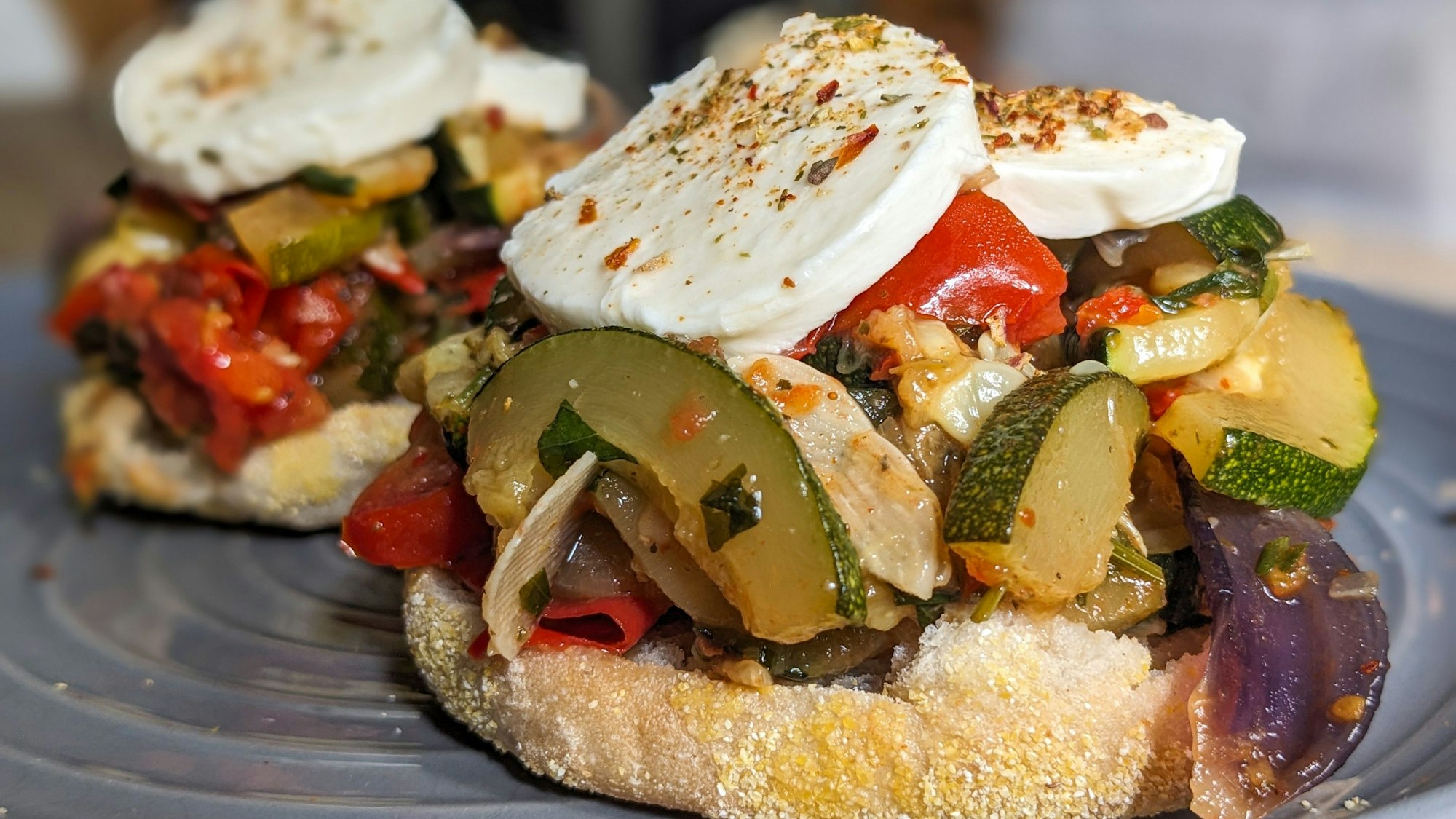 Auf einem Toastbrötchen liegt das angebratene Zucchini-Tomaten-Gemüse sowie Mozzarellascheiben.