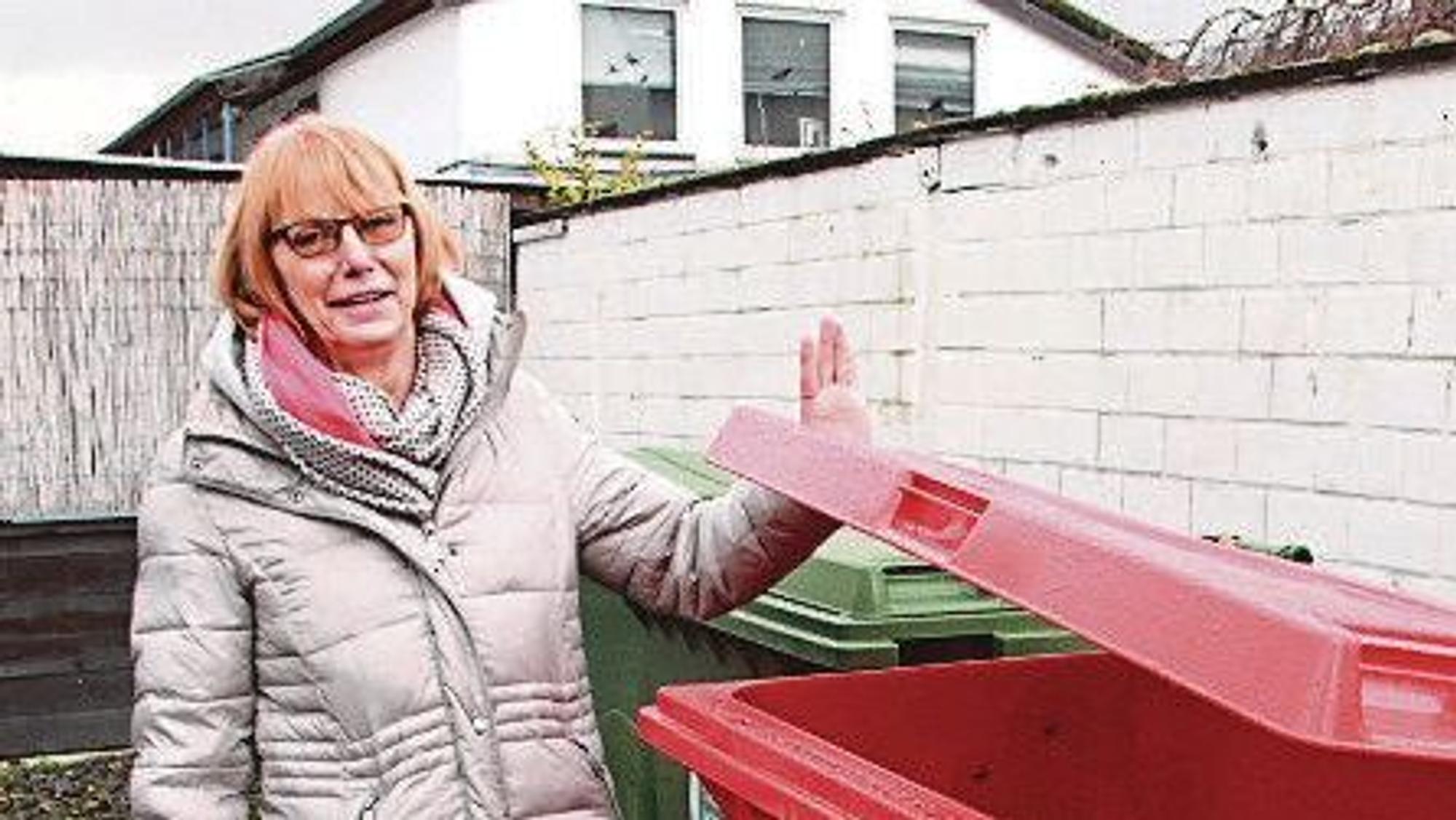 Eine Frau mit rötlichen Haaren steht neben einem roten Kunststoffcontainer. Sie trägt einen Wintermantel.