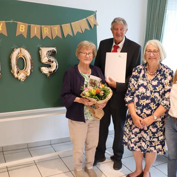 Gruppenfoto mit einer 150 aus Luftballons im Hintergrund. Eine ältere Frau, die Geburtstag hat, hält einen Blumenstrauß in den Händen.