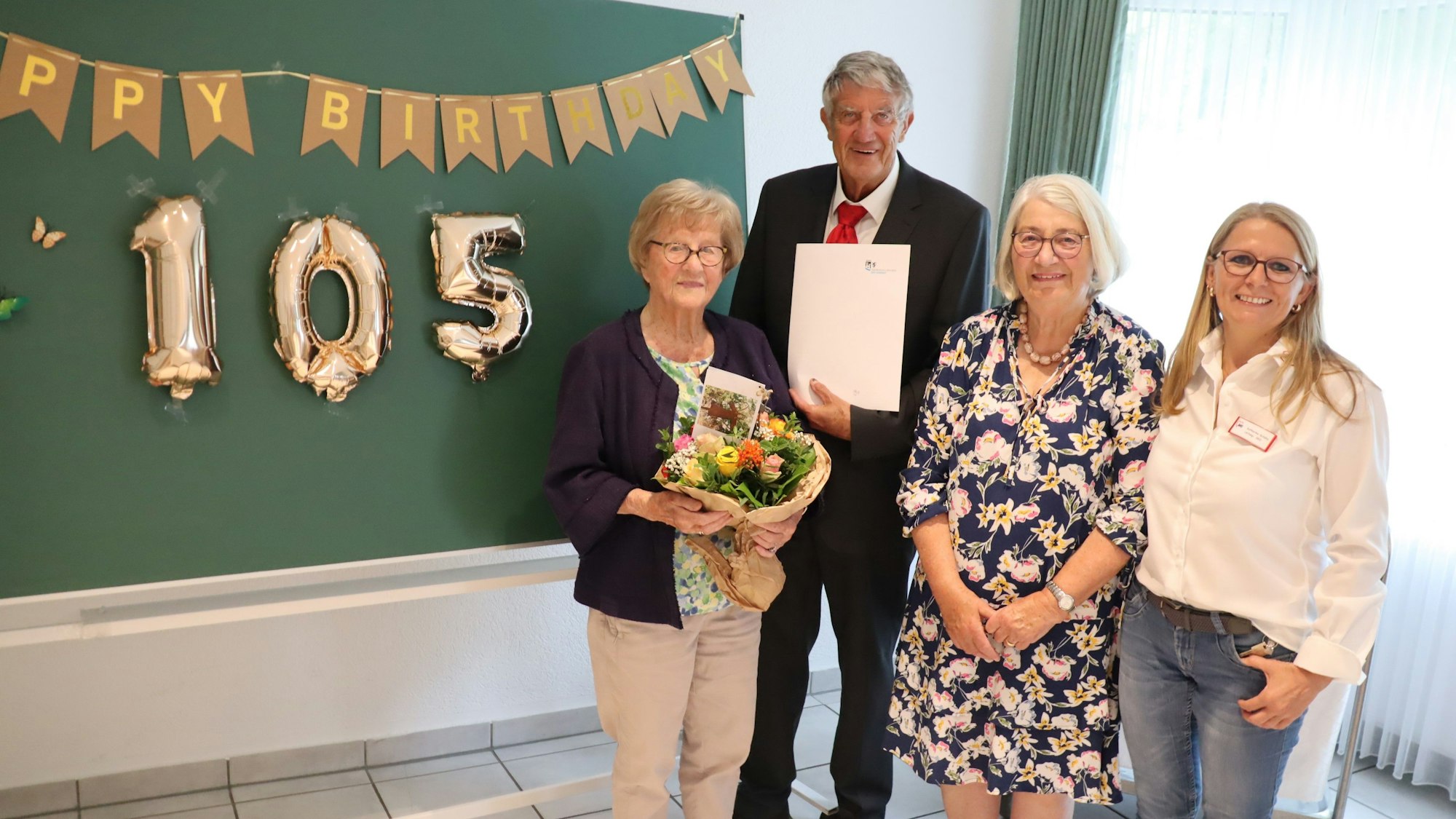 Gruppenfoto mit einer 150 aus Luftballons im Hintergrund. Eine ältere Frau, die Geburtstag hat, hält einen Blumenstrauß in den Händen.
