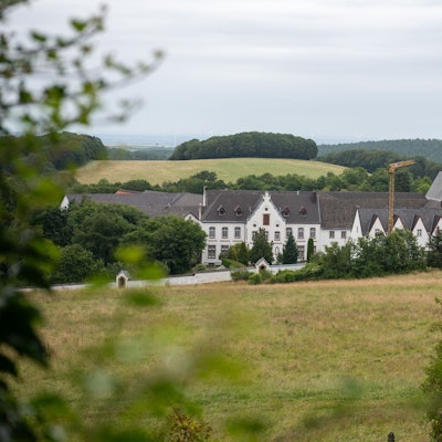 Blick auf das Kloster Mariawald, ringsumher sind Hügel und Wald zu sehen.