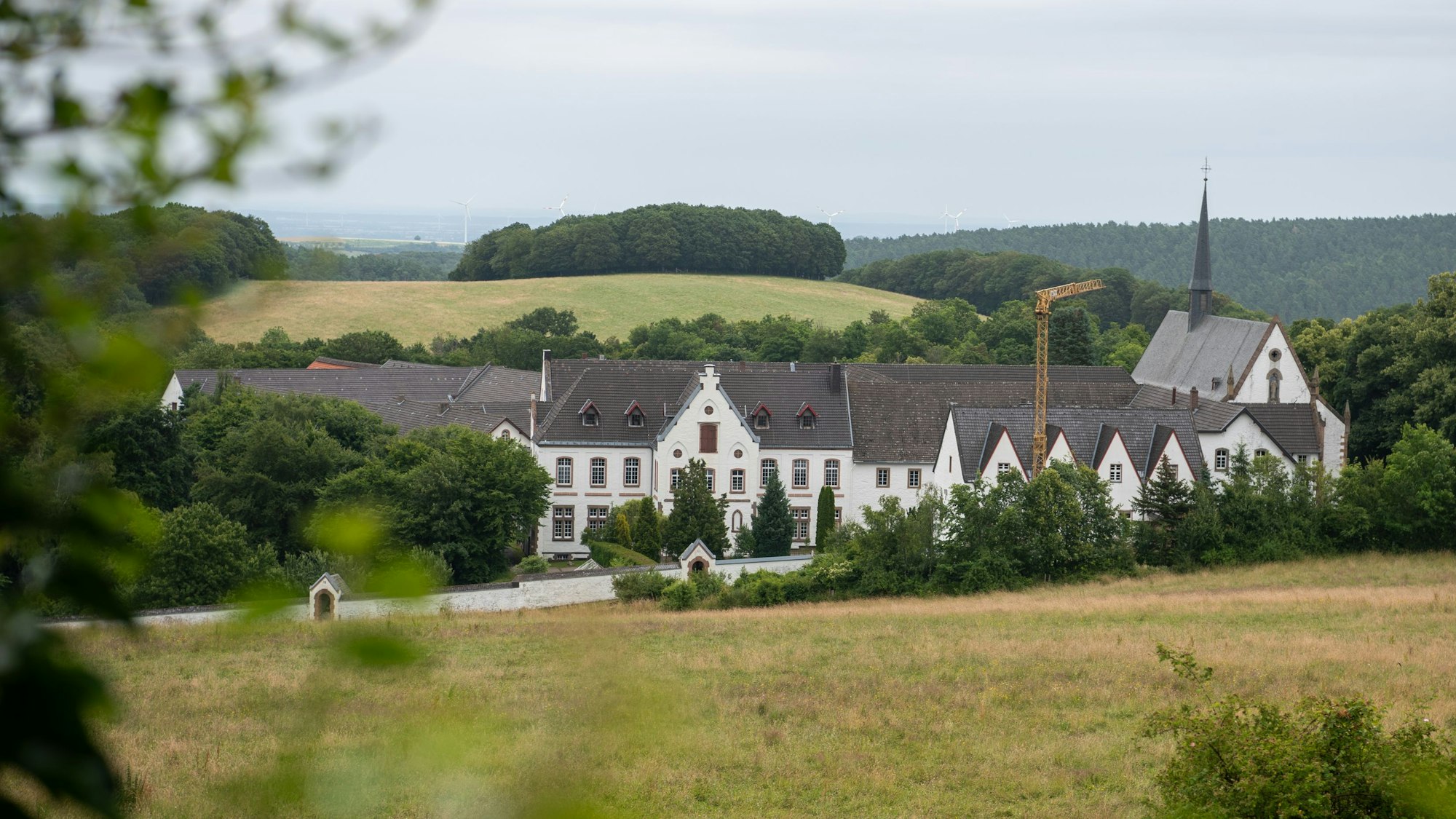 Blick auf das Kloster Mariawald, ringsumher sind Hügel und Wald zu sehen.