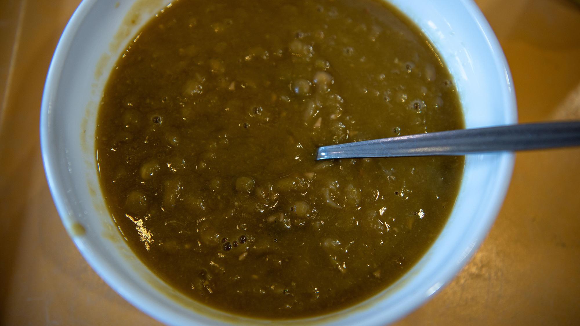 In einer weißen Schüssel befindet sich braun-grüne Erbsensuppe. In der Schüssel steckt ein Löffel.