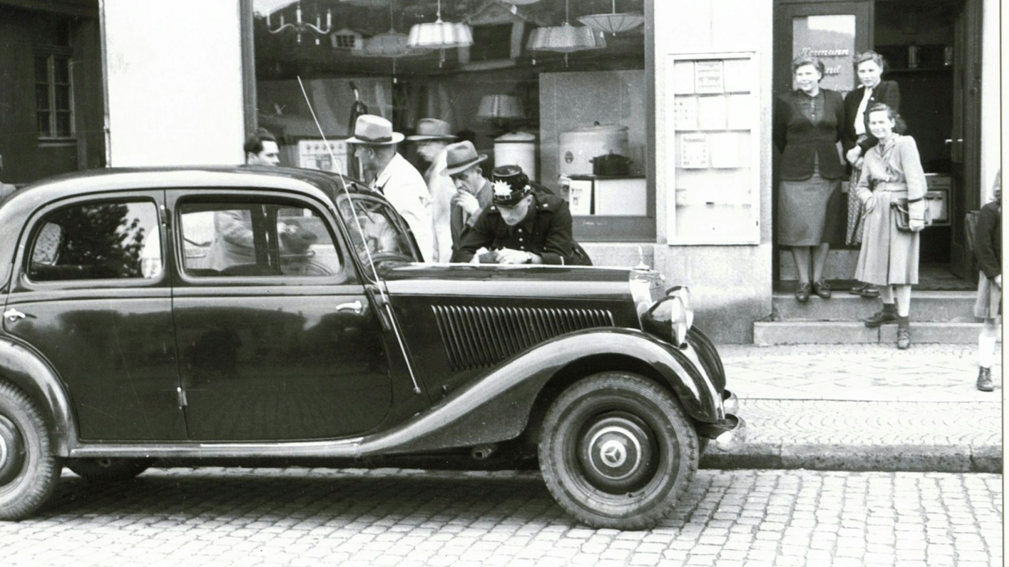 Ein Polizist schreibt auf der Motorhaube einer großen Limousine ein Strafmandat.