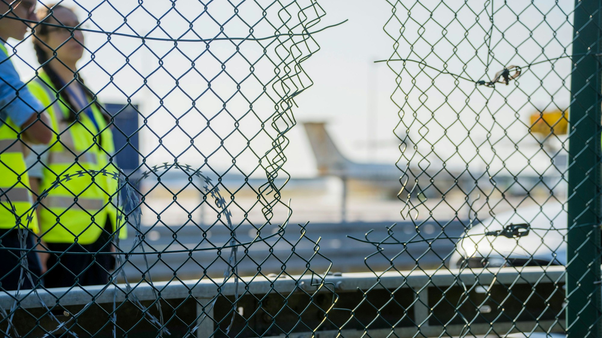 Fraport-Mitarbeiter stehen an dem zerstörten Zaunabschnitt, durch den die Klima-Aktivisten auf das Flughafengelände eingedrungen sind.