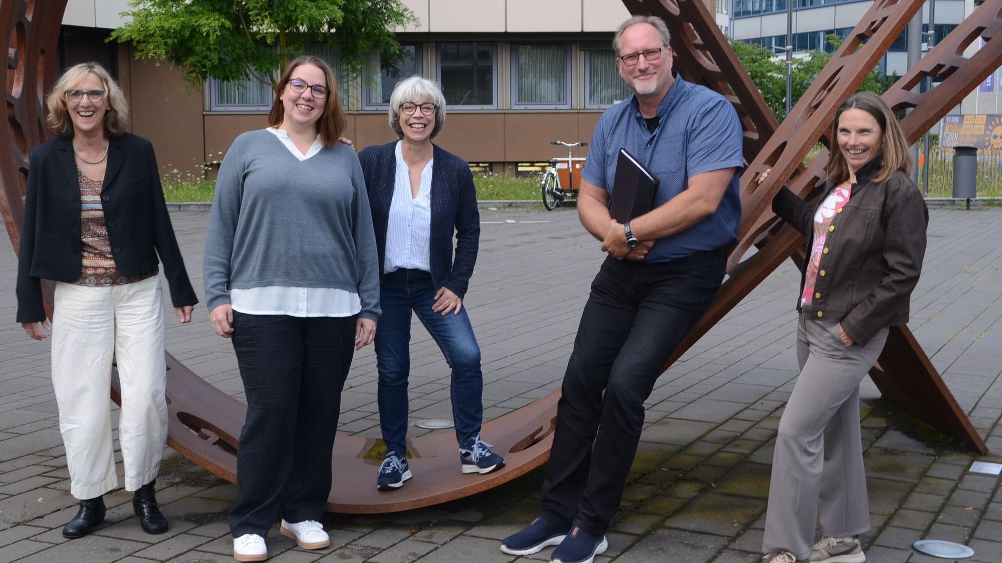 Ein Mann und vier Frauen haben sich um ein Kunstwerk zum Gruppenfoto aufgestellt.