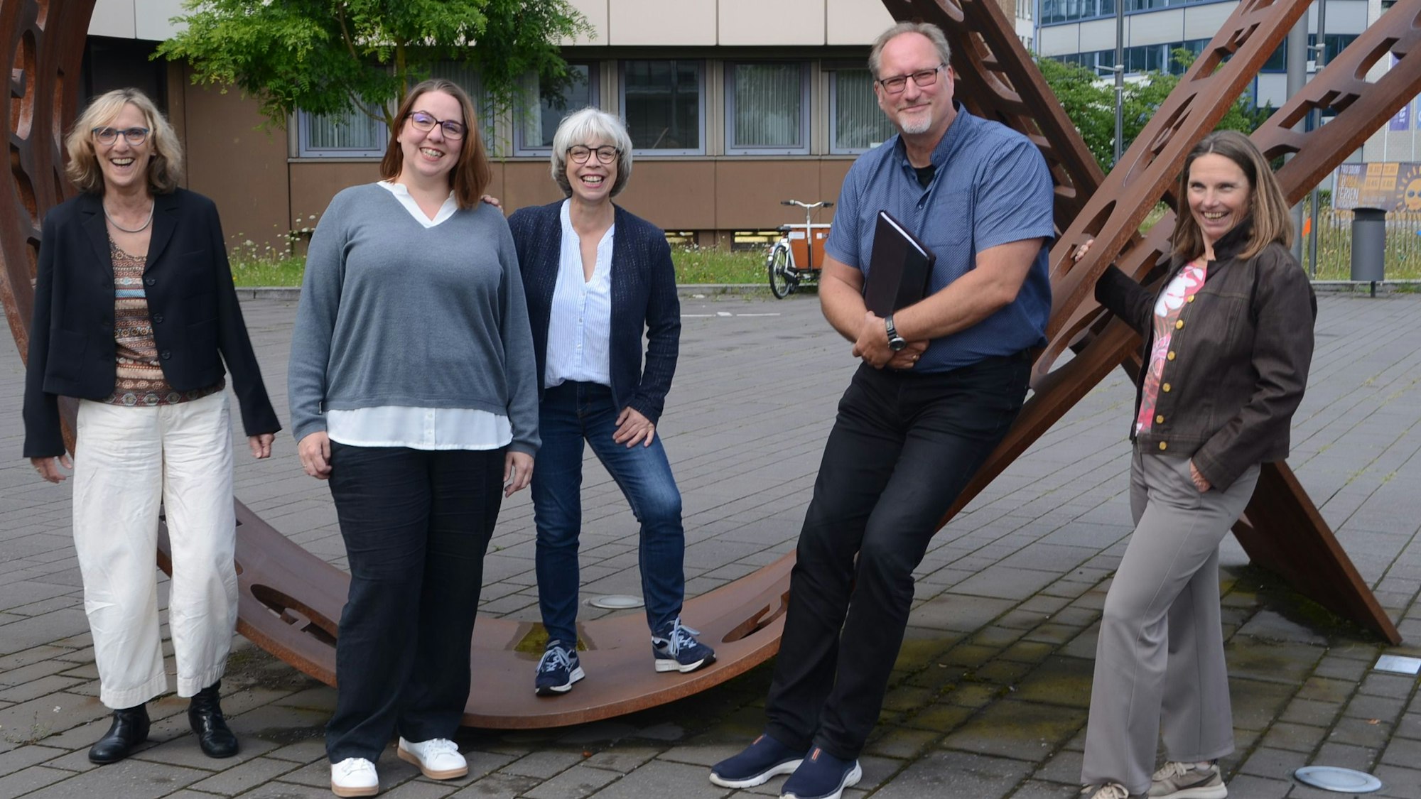 Ein Mann und vier Frauen haben sich um ein Kunstwerk zum Gruppenfoto aufgestellt.