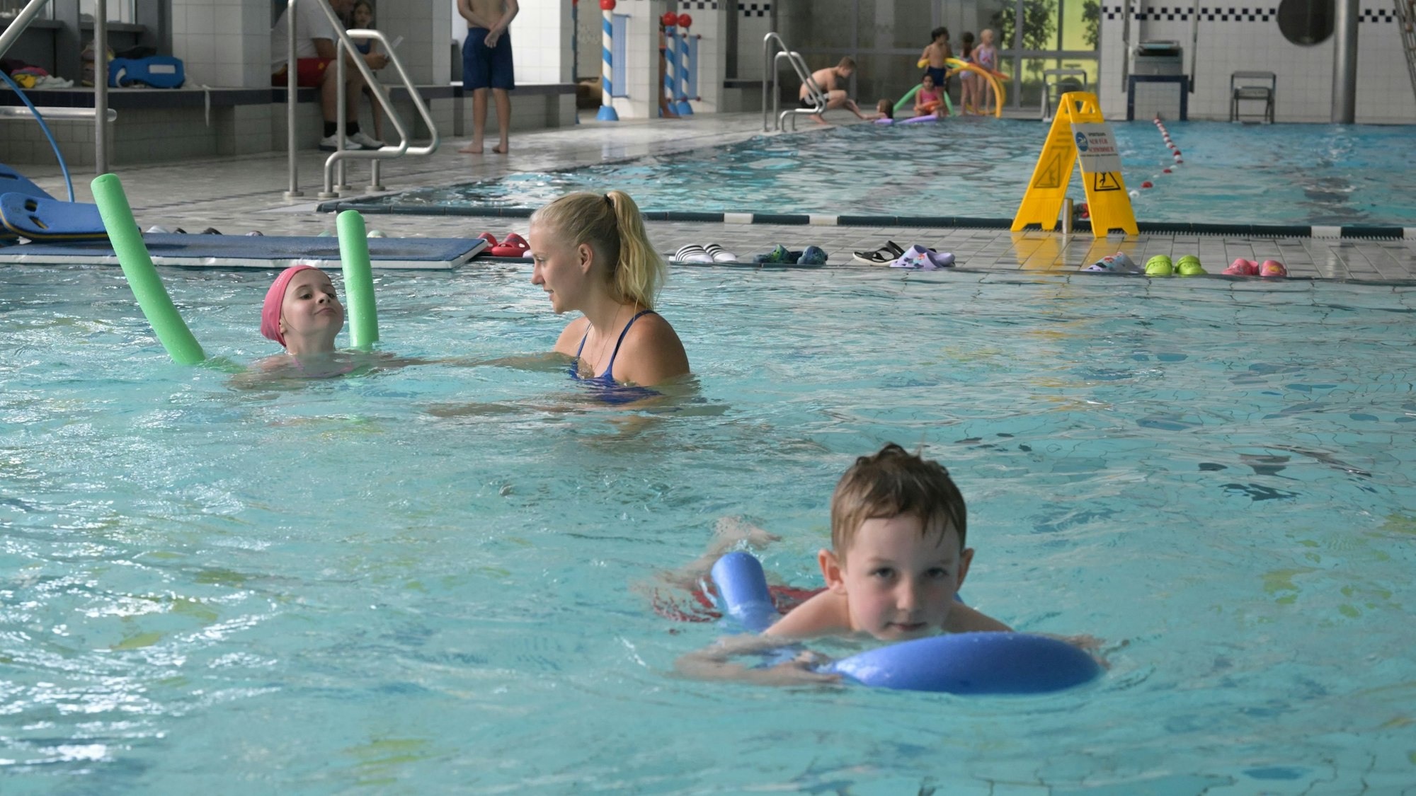 Die Kinder schwimmen mit einer Schwimmnudel.