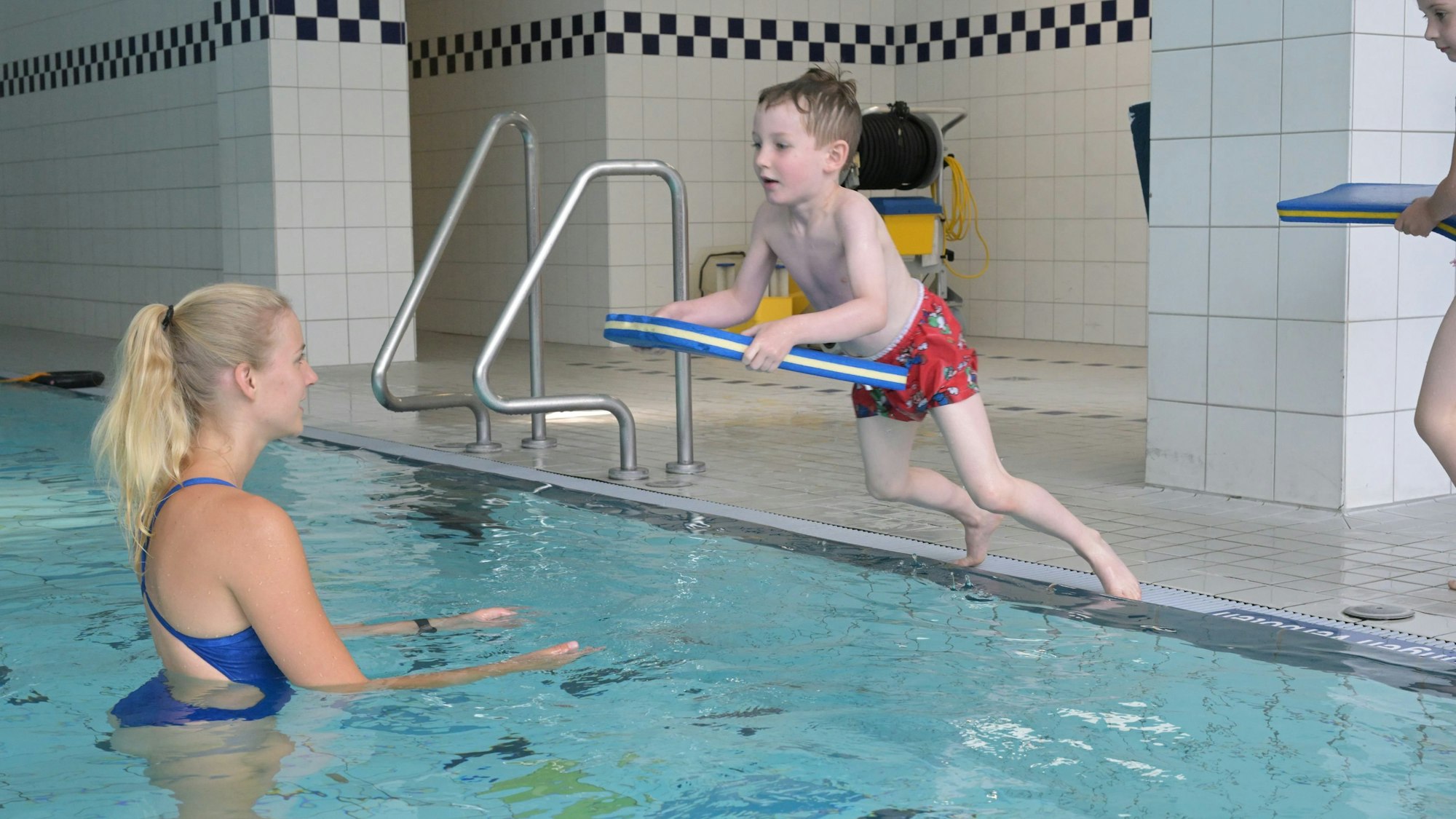 Adrian springt mit einem Schwimmbrett vom Beckenrand.