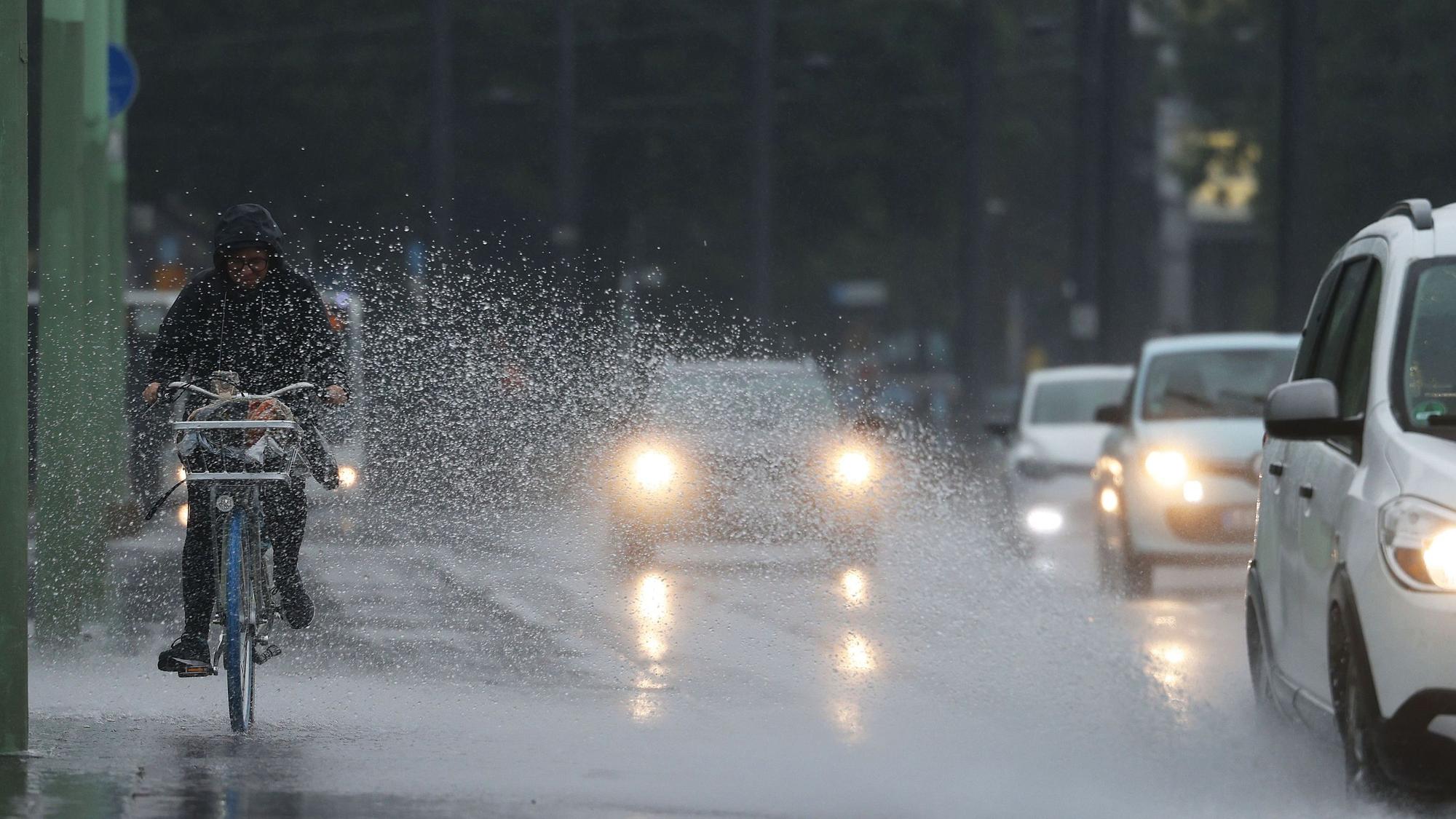 Eine Radfahrerin wird vom Spritzwasser eines Autos getroffen. In Nordrhein-Westfalen werden in den nächsten Tagen Gewitter und viel Regen erwartet.