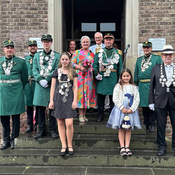 Männer und Frauen in Kleidern und Uniformen stehen vor einem Gebäude.