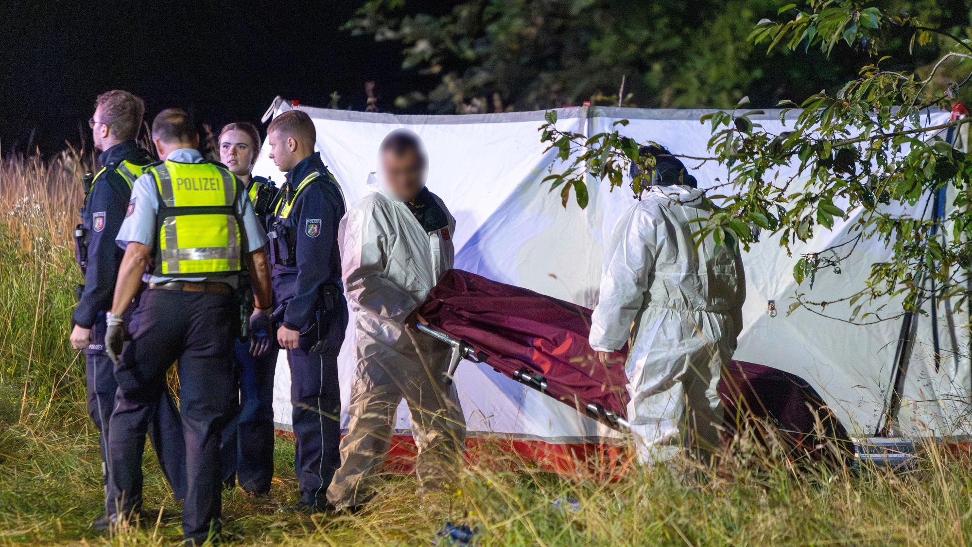 Einsatzkräfte der Polizei stehen nach einem Unfall im Grünstreifen der A44, Mitarbeiter eines Bestattungsunternehmens transportieren die Leiche eines der Unfallopfer ab.