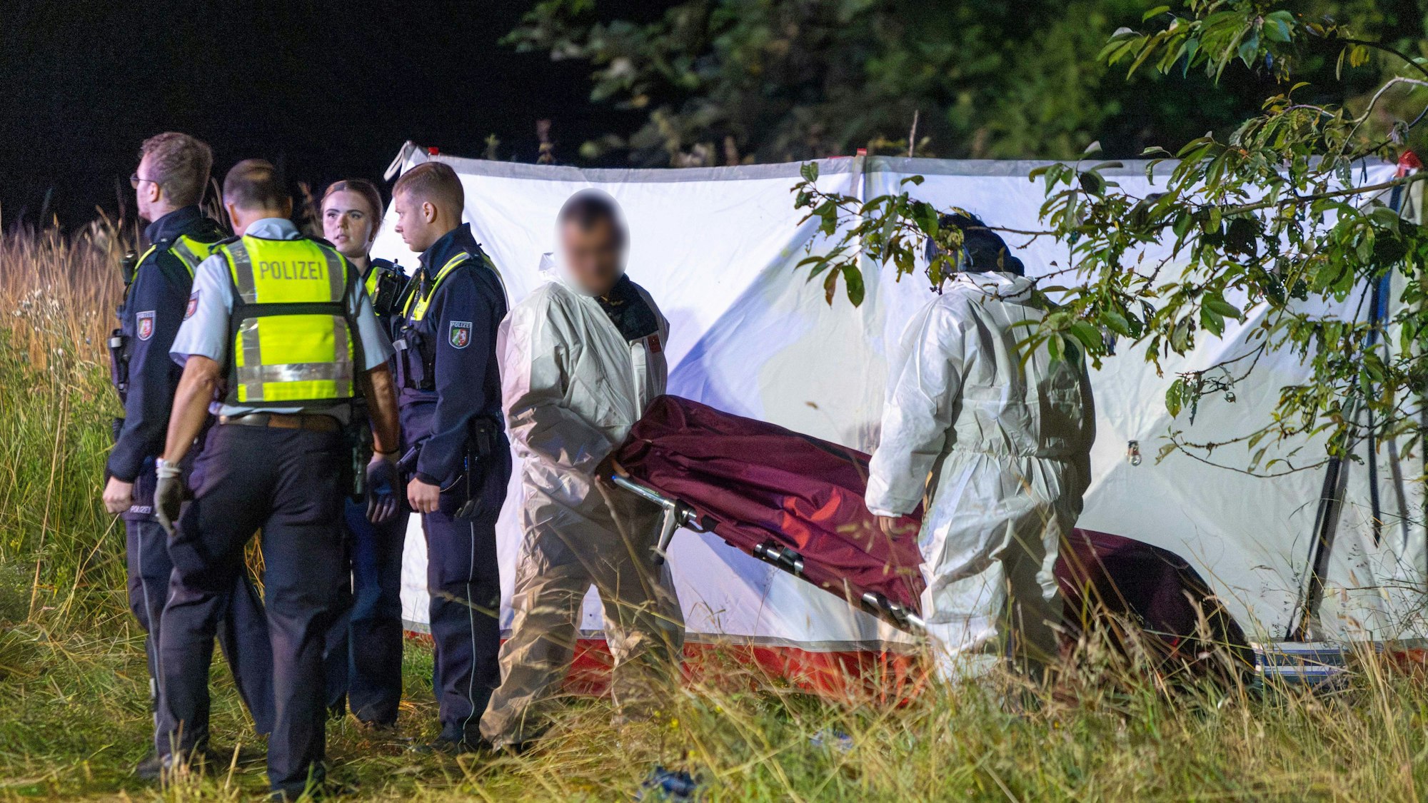 Einsatzkräfte der Polizei stehen nach einem Unfall im Grünstreifen der A44, Mitarbeiter eines Bestattungsunternehmens transportieren die Leiche eines der Unfallopfer ab.