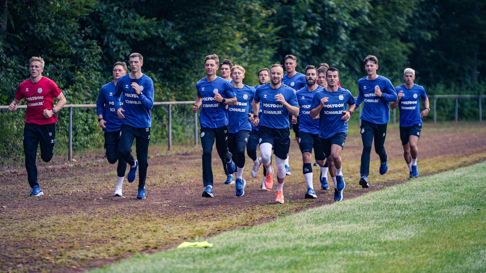 Die Handballer des VfL Gummersbach laufen als Gruppe um einen Sportplatz.