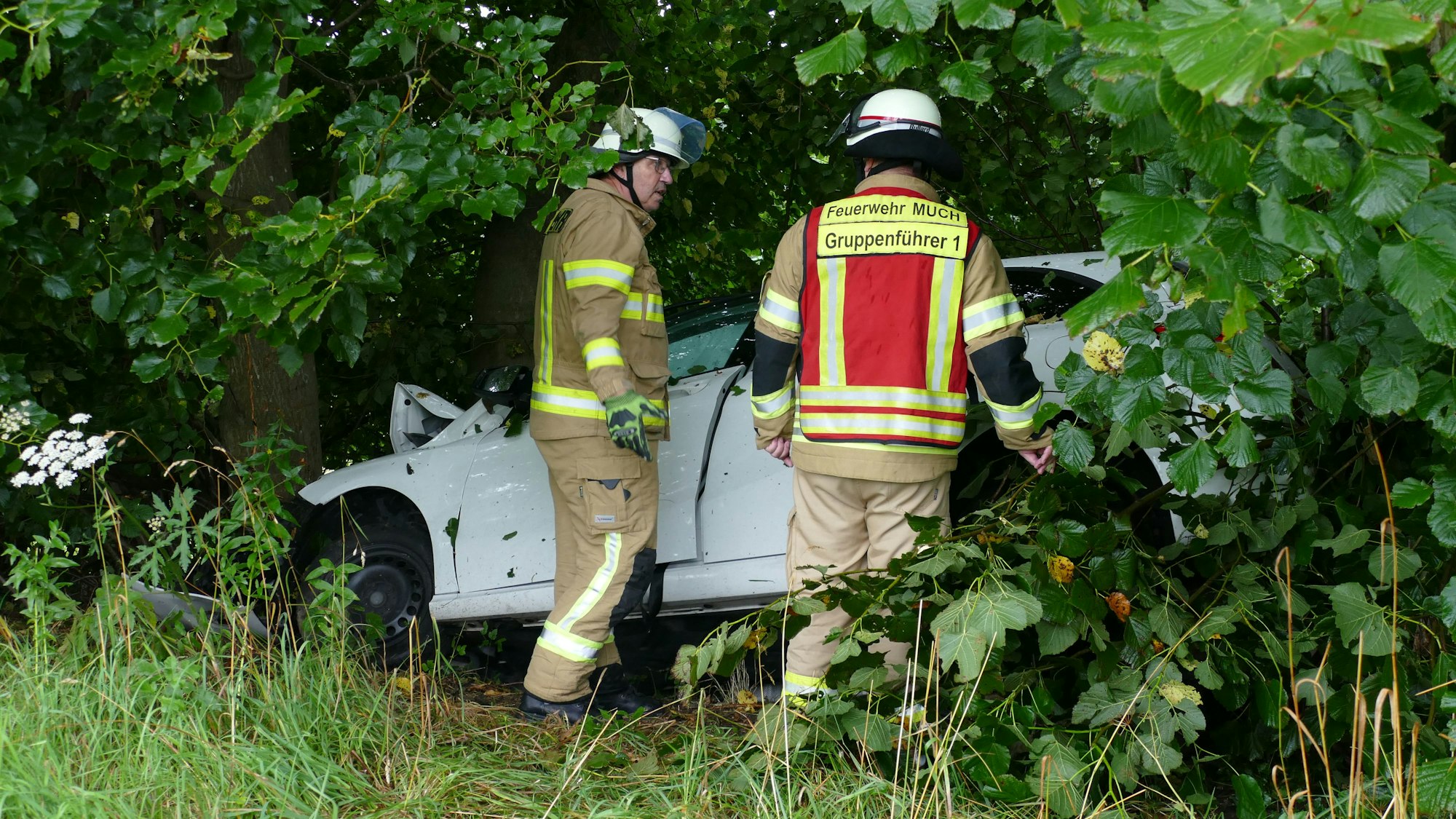 Feuerwehrleute stehen nebem dem Auto, das gegen den Baum geprallt war.
