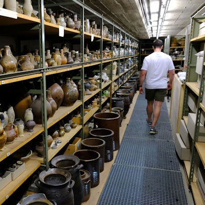 Töpferwaren aus dem Rheinland lagern in Regalen des Kommerner Museums-Depots. Ein Mitarbeiter geht daran vorbei.