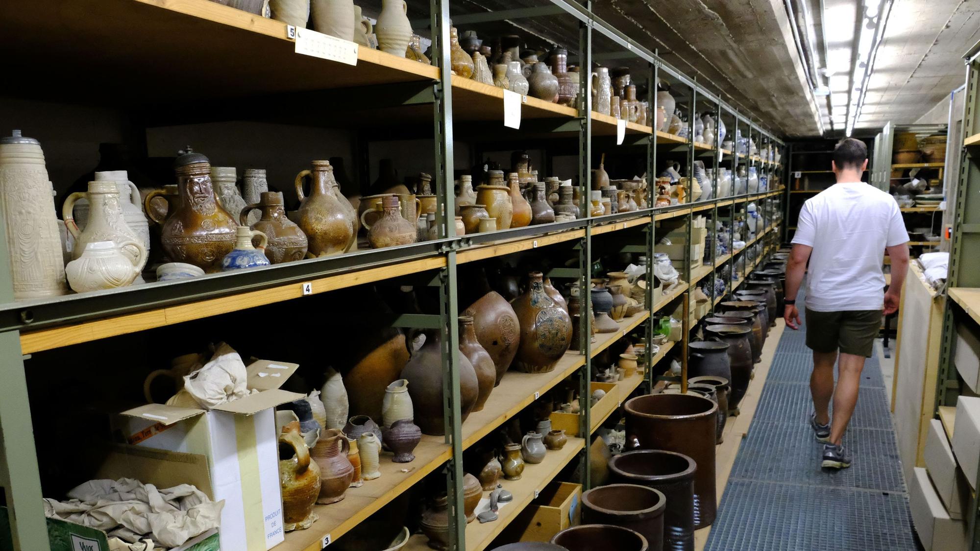 Töpferwaren aus dem Rheinland lagern in Regalen des Kommerner Museums-Depots. Ein Mitarbeiter geht daran vorbei.
