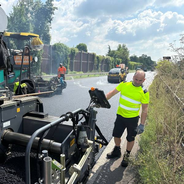 Arbeiter bringen Asphalt auf einer Straße auf.