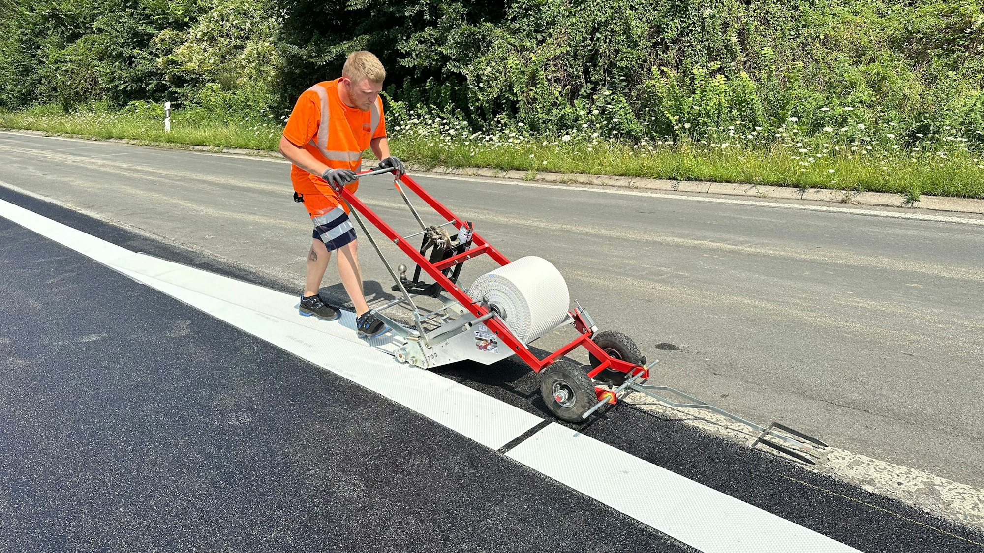 Ein Bauarbeiter schiebt eine Karre über eine Baustelle. Mit Folie werden Fahrspuren markiert.