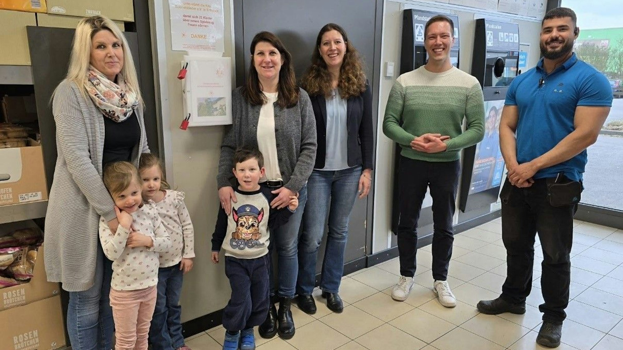 Frauen, Männer und Kinder stehen in einer Aldi-Filiale neben einem Pfandautomaten.