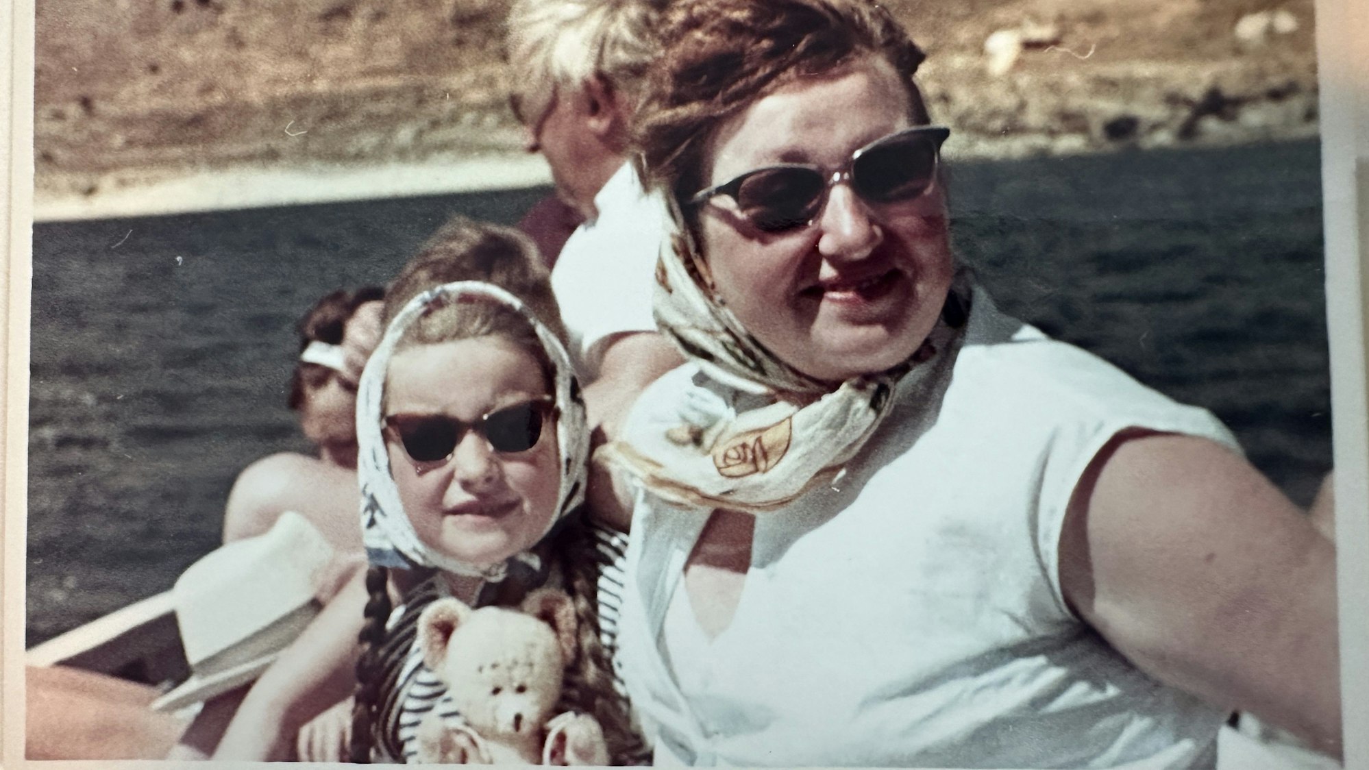 Ein altes Urlaubsfoto von einer Mutter und ihrer Tochter. Die Tochter hält einen Teddy in den Händen.