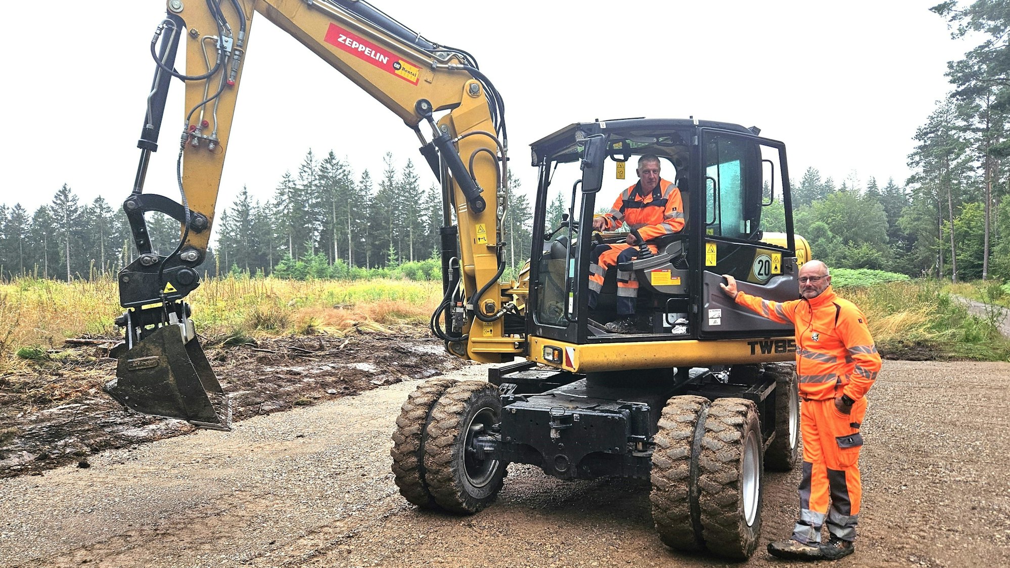 Ralf Mertens sitzt in seinem Bagger, Michael Dreßen steht rechts daneben.