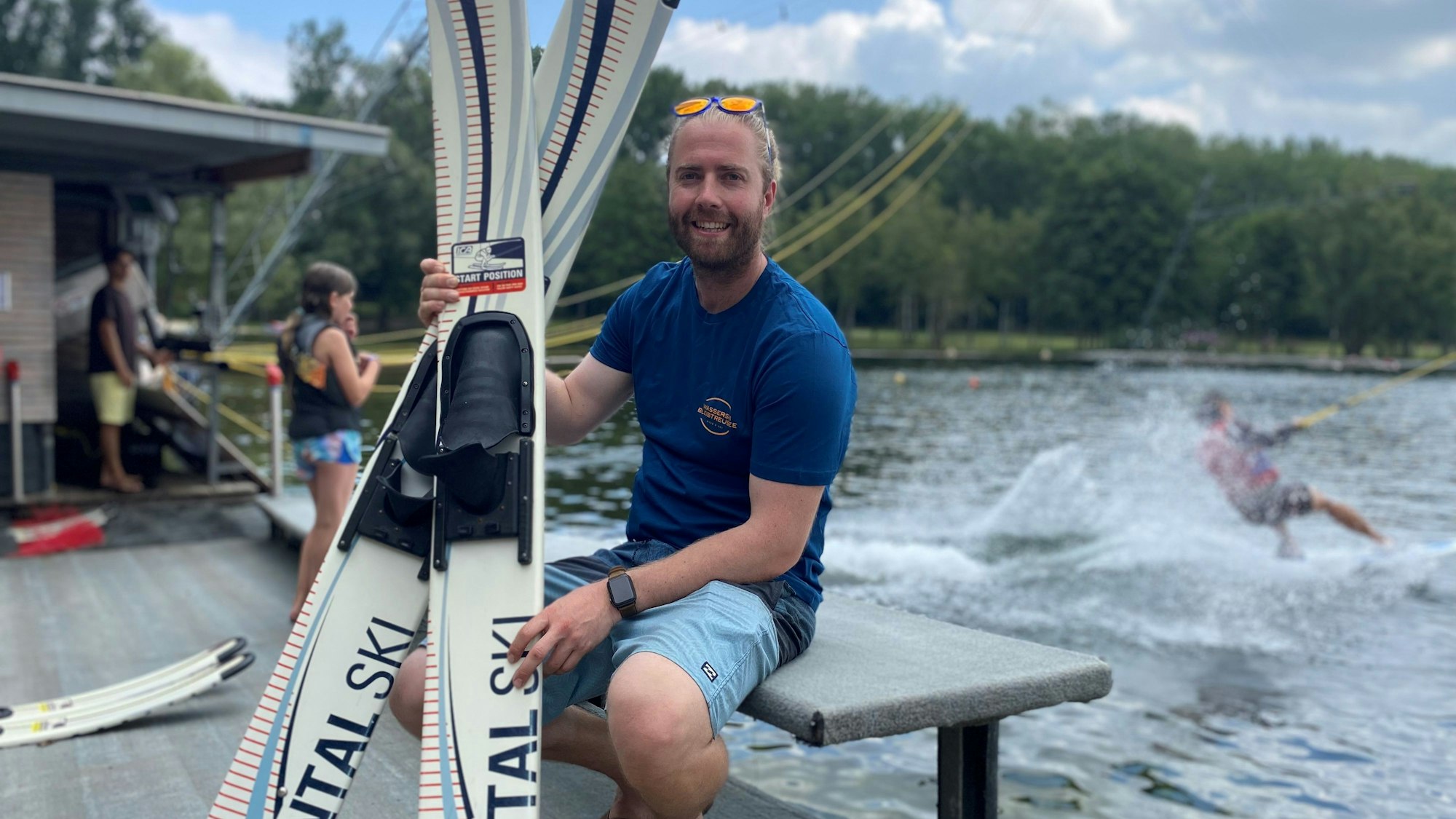Ein Mann sitzt mit Wasserski an einem See.