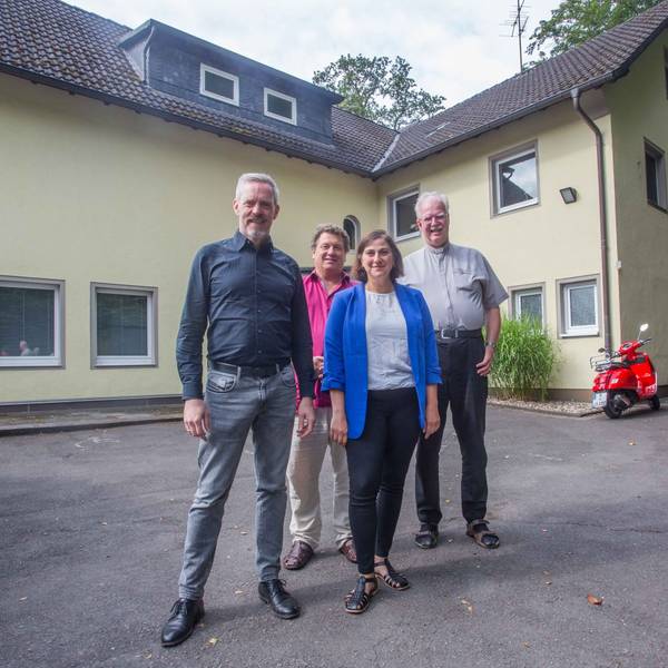 Drei Herren und eine Dame vor einem Haus.