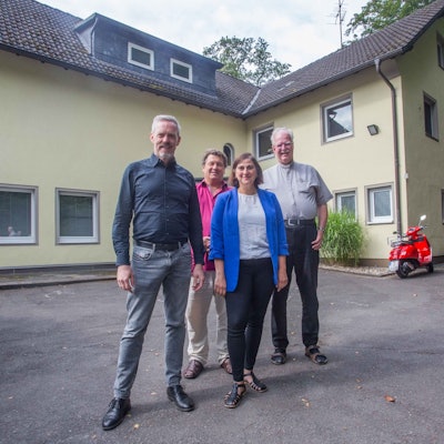 Drei Herren und eine Dame vor einem Haus.