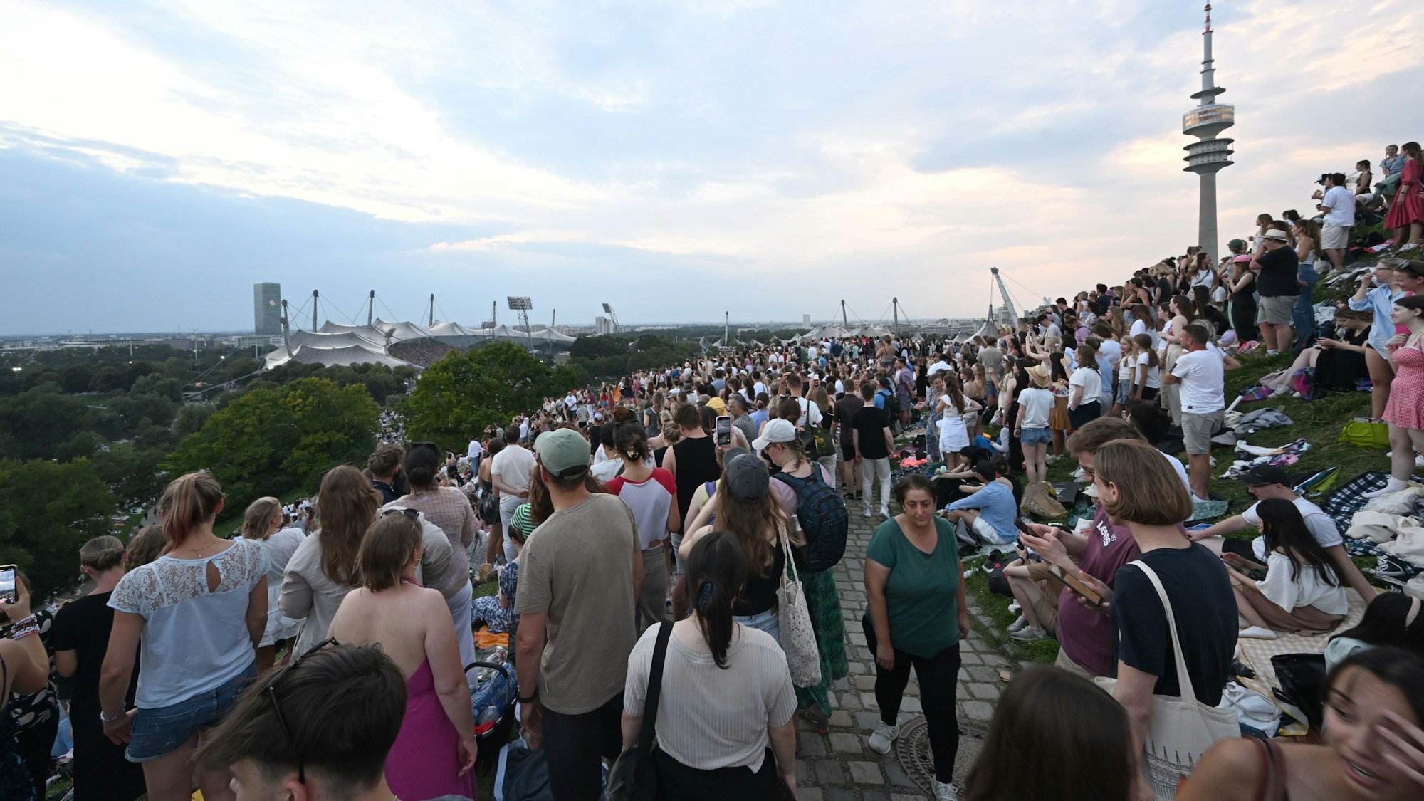 Fans stehen während des Taylor Swift Konzerts auf dem Olympiaberg bei Abenddämmerung.