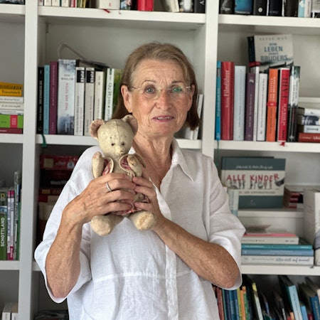 Eine ältere Frau hält einen älteren Teddybären aus ihrer Kindheit in den Händen.