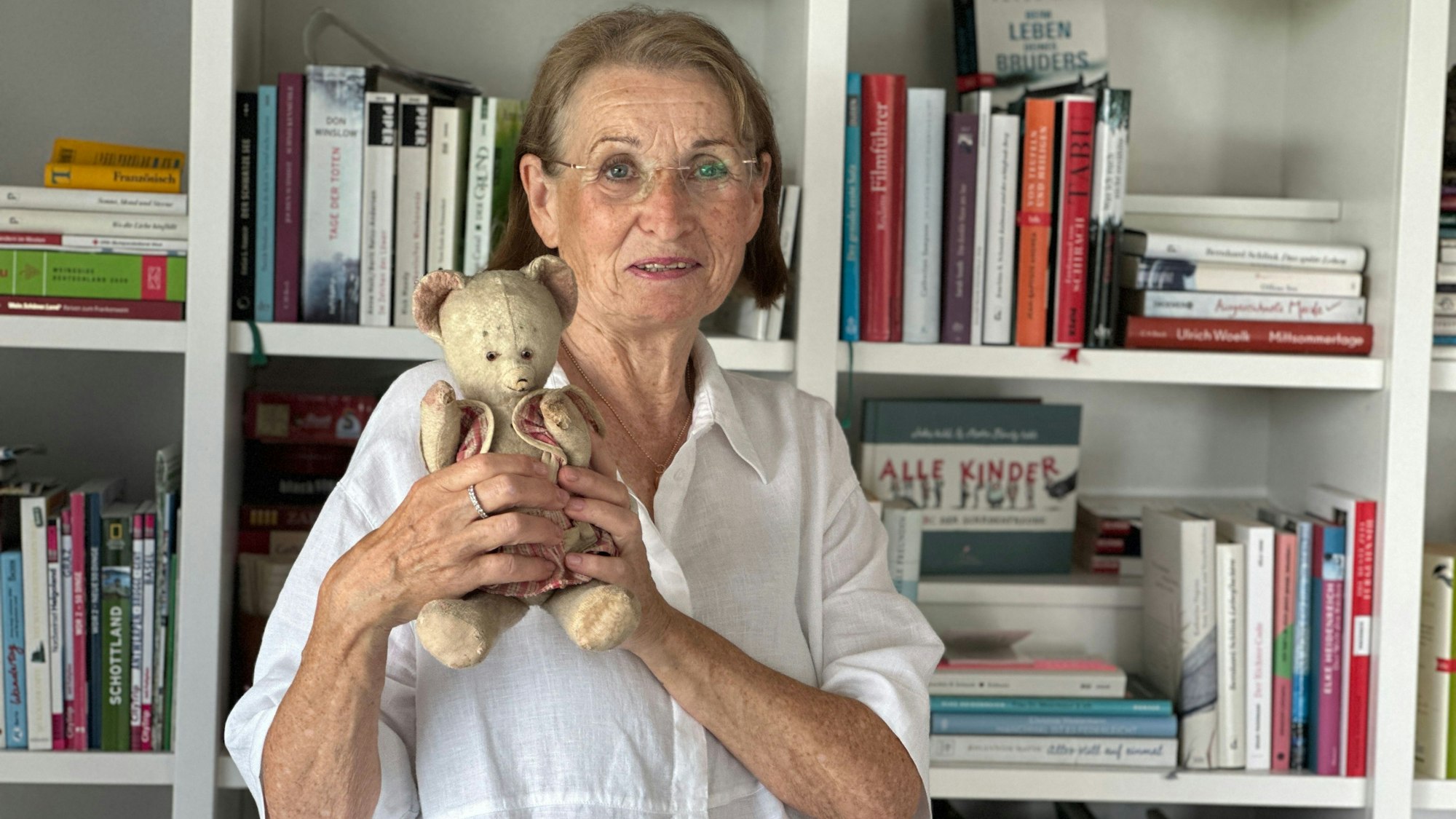 Eine ältere Frau hält einen älteren Teddybären aus ihrer Kindheit in den Händen.