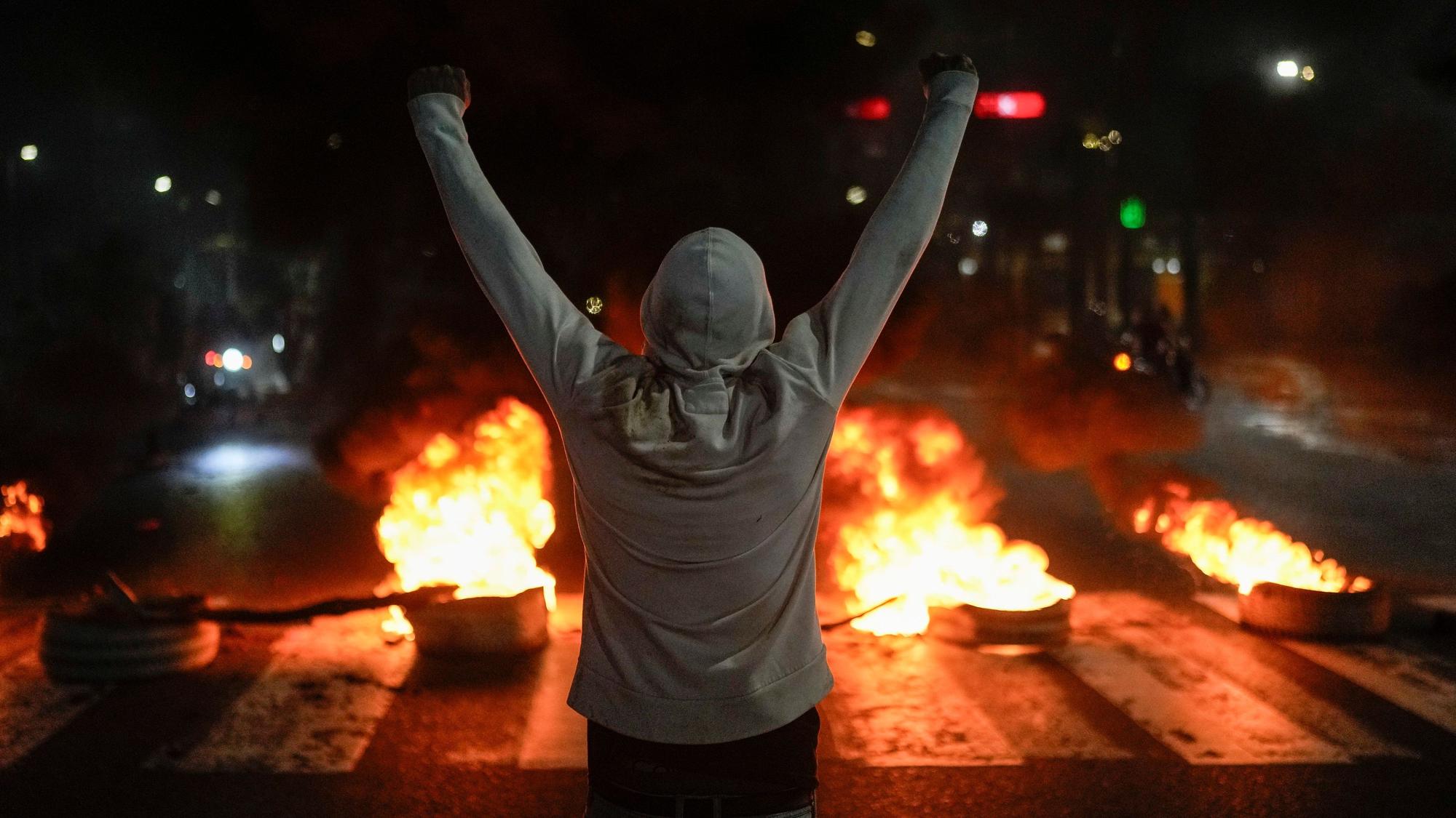 Ein Demonstrant hebt seine Arme vor brennenden Reifen, am Tag nach der Präsidentschaftswahl.