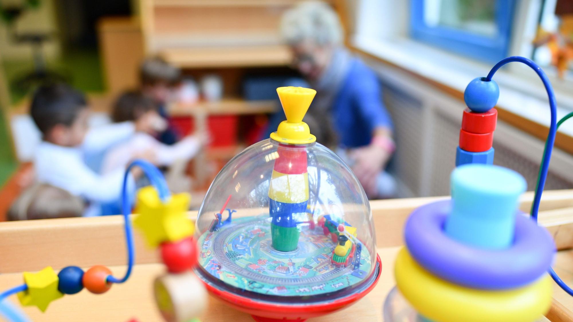 Eine Erzieherin spielt in einer Kita mit Kindern. Im Vordergrund steht Spielzeug.