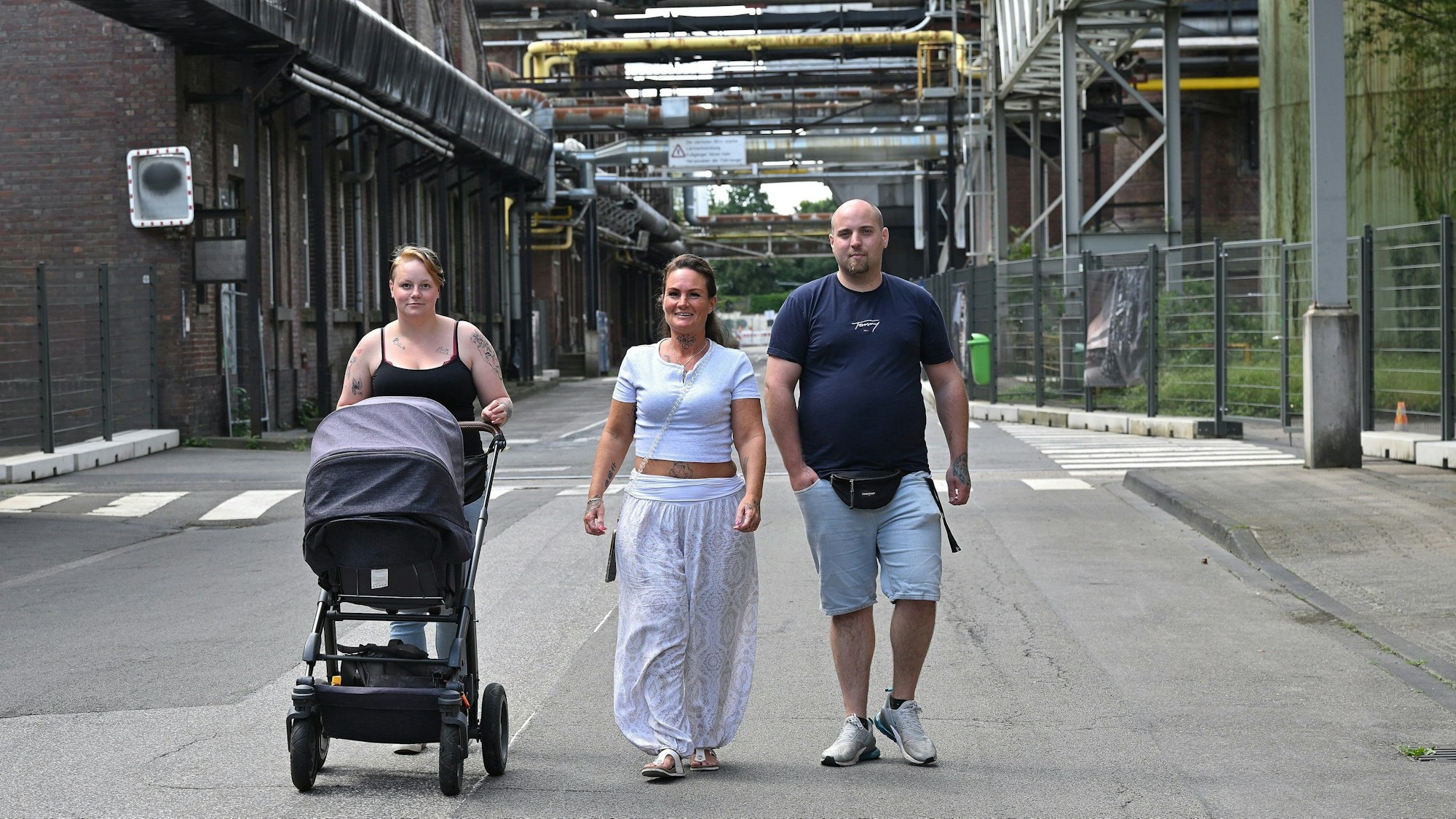 Drei Menschen laufen über das Zanders-Geläne, eine Frau schiebt einen Kinderwagen.
