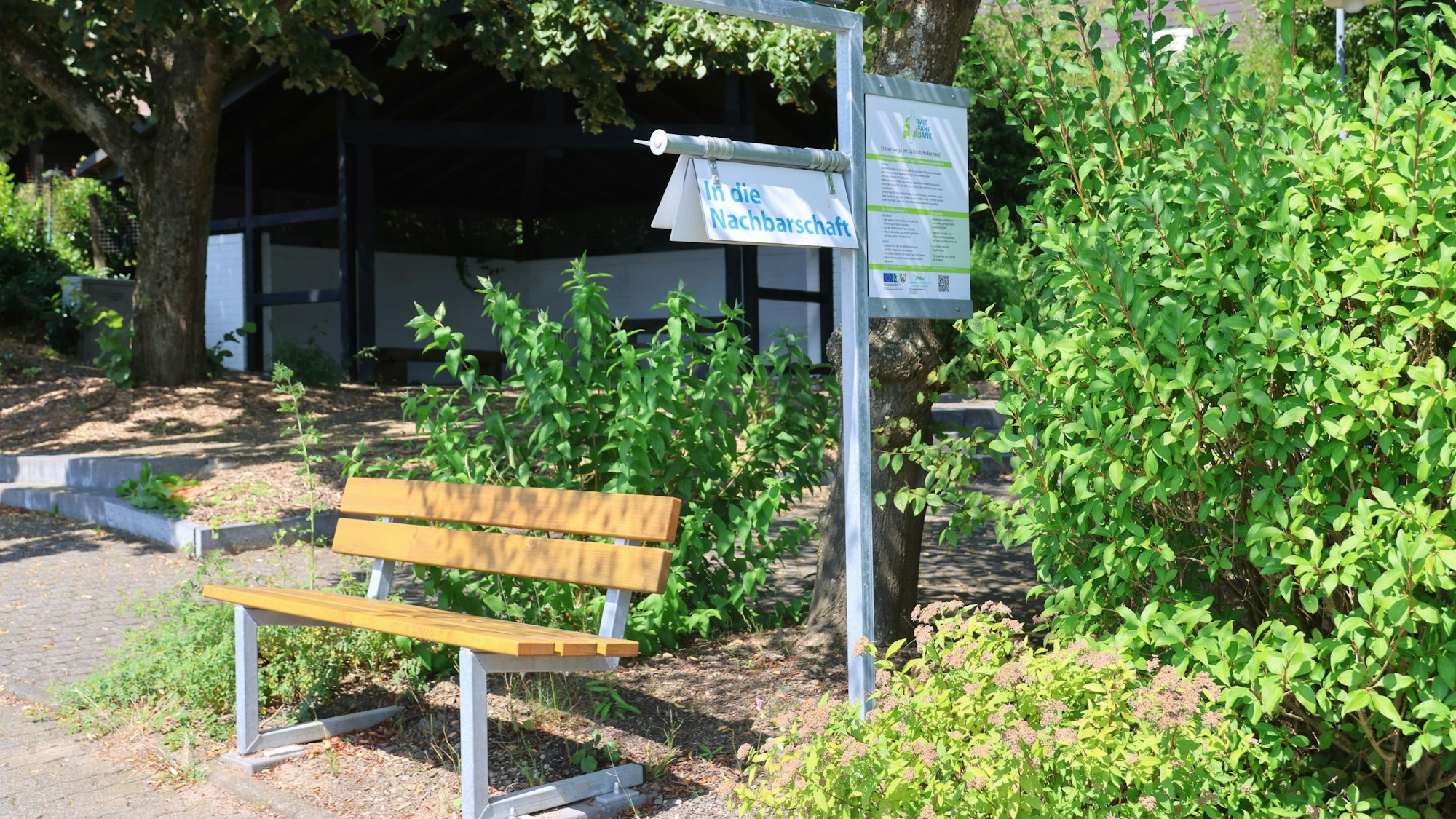 Eine leere Bank, daneben ein Schild mit der Aufschrift „In die Nachbarschaft“.
