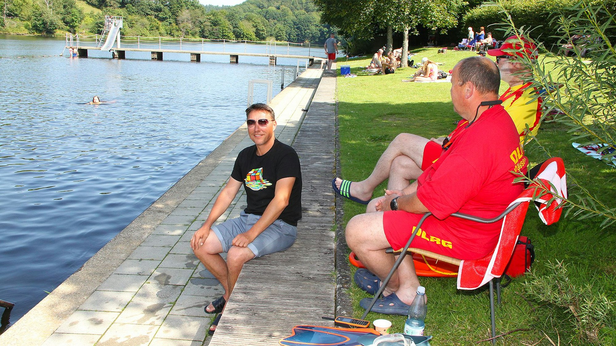 Drei Männer sitzen am Steg des Naturerlebnisbads Einruhr am Rursee.