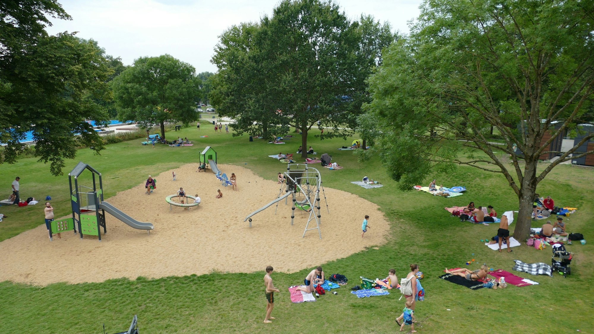 Menschen sitzen auf einer Liegewiese im Freibad.