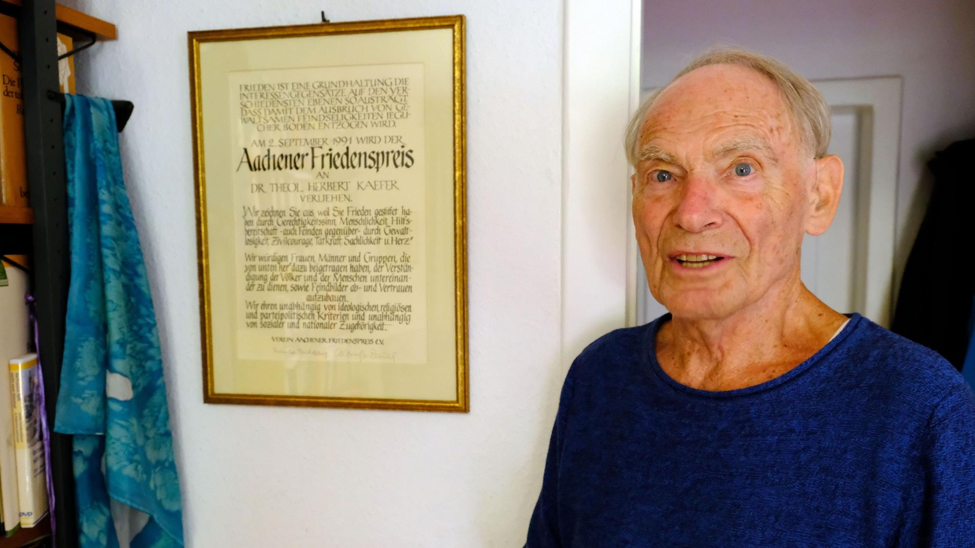 Dr. Herbert Kaefer neben der Urkunde des Aachener Friedenspreises, die in einem Rahmen an der Wand seines Wohnzimmers hängt.