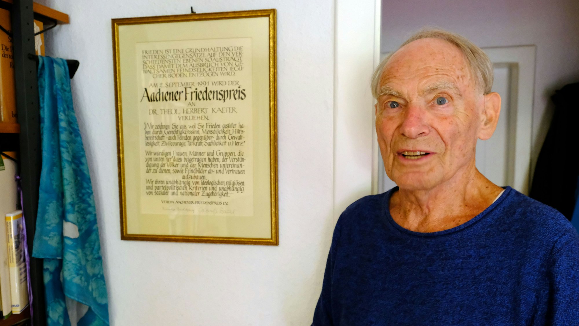 Dr. Herbert Kaefer neben der Urkunde des Aachener Friedenspreises, die in einem Rahmen an der Wand seines Wohnzimmers hängt.