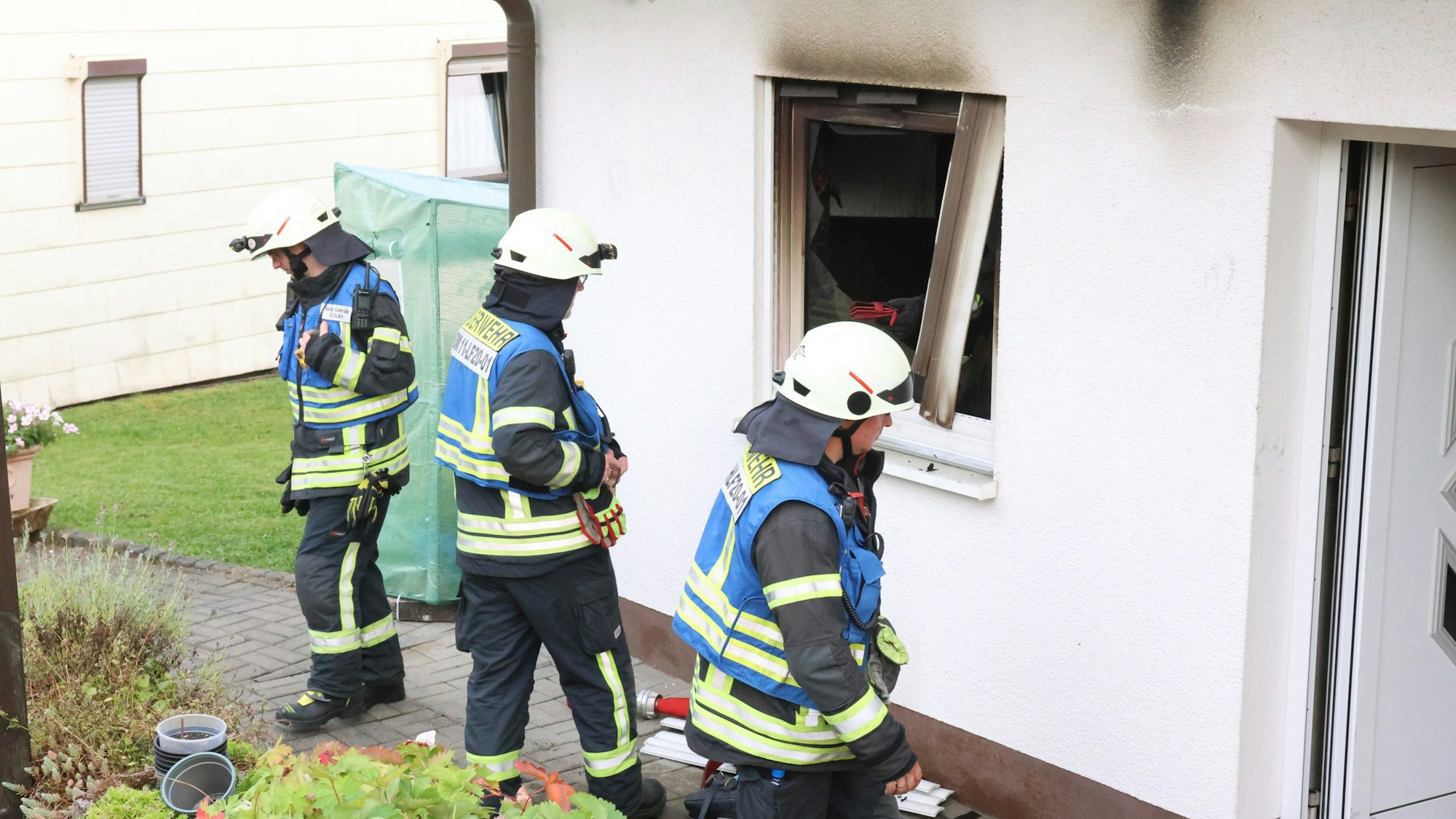 Drei Feuerwehrleute stehen vor einem Haus, in dem es zuvor gebrannt hat.