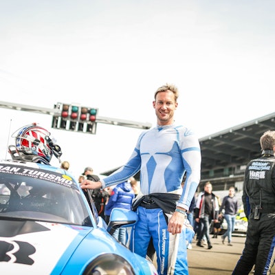 Der Rennfahrer Peter Terting steht neben seinem Rennauto. Sein Helm liegt auf dem Dach des Wagens.