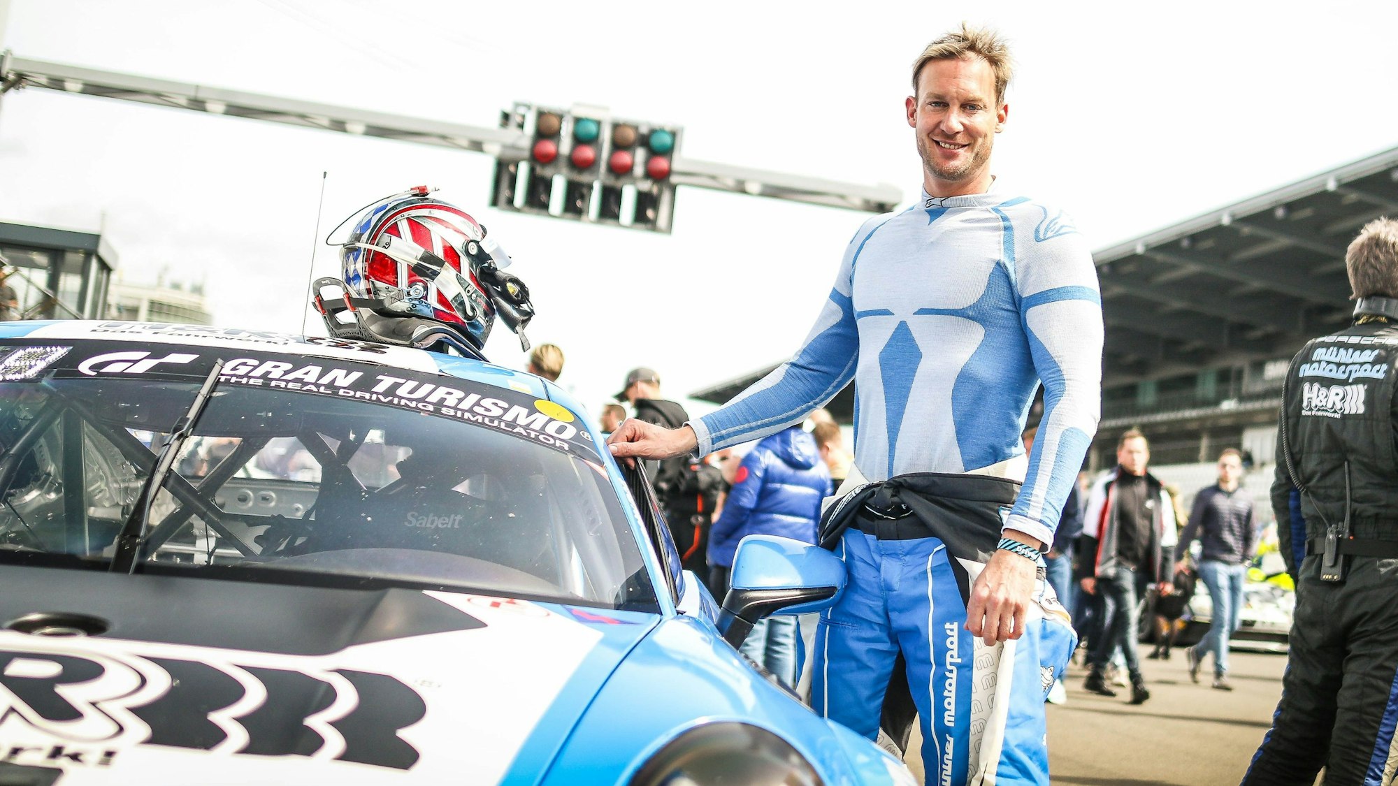 Der Rennfahrer Peter Terting steht neben seinem Rennauto. Sein Helm liegt auf dem Dach des Wagens.