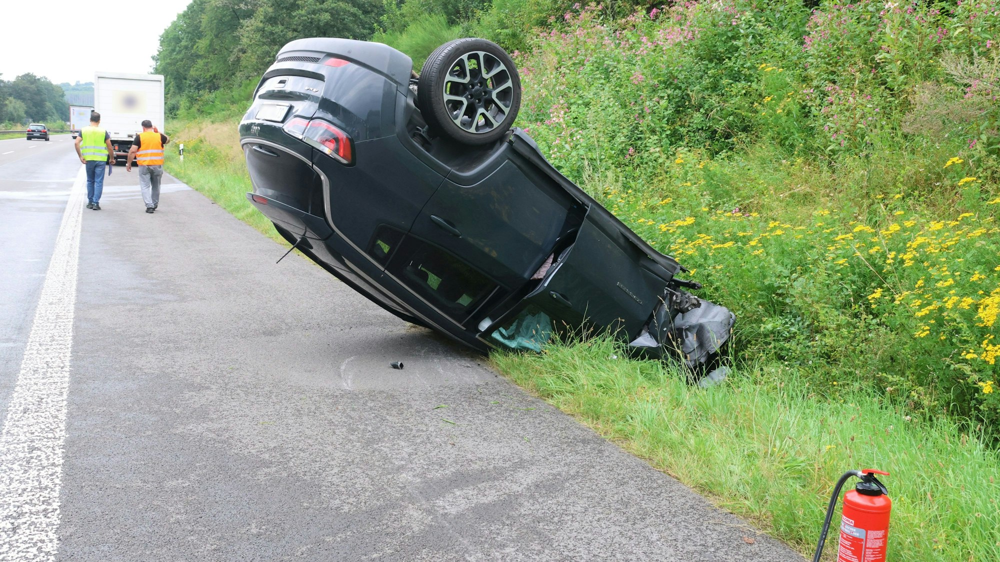 Ein Auto liegt auf einem Standstreifen einer Autobahn auf dem Dach.
