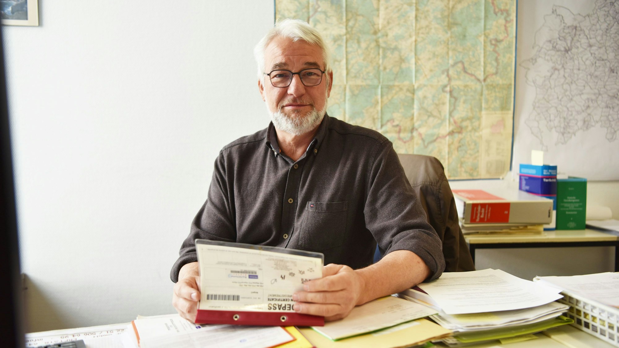 Dr. Jochen Weins sitzt an seinem Schreibtisch, in der Hand einen Pferdepass.