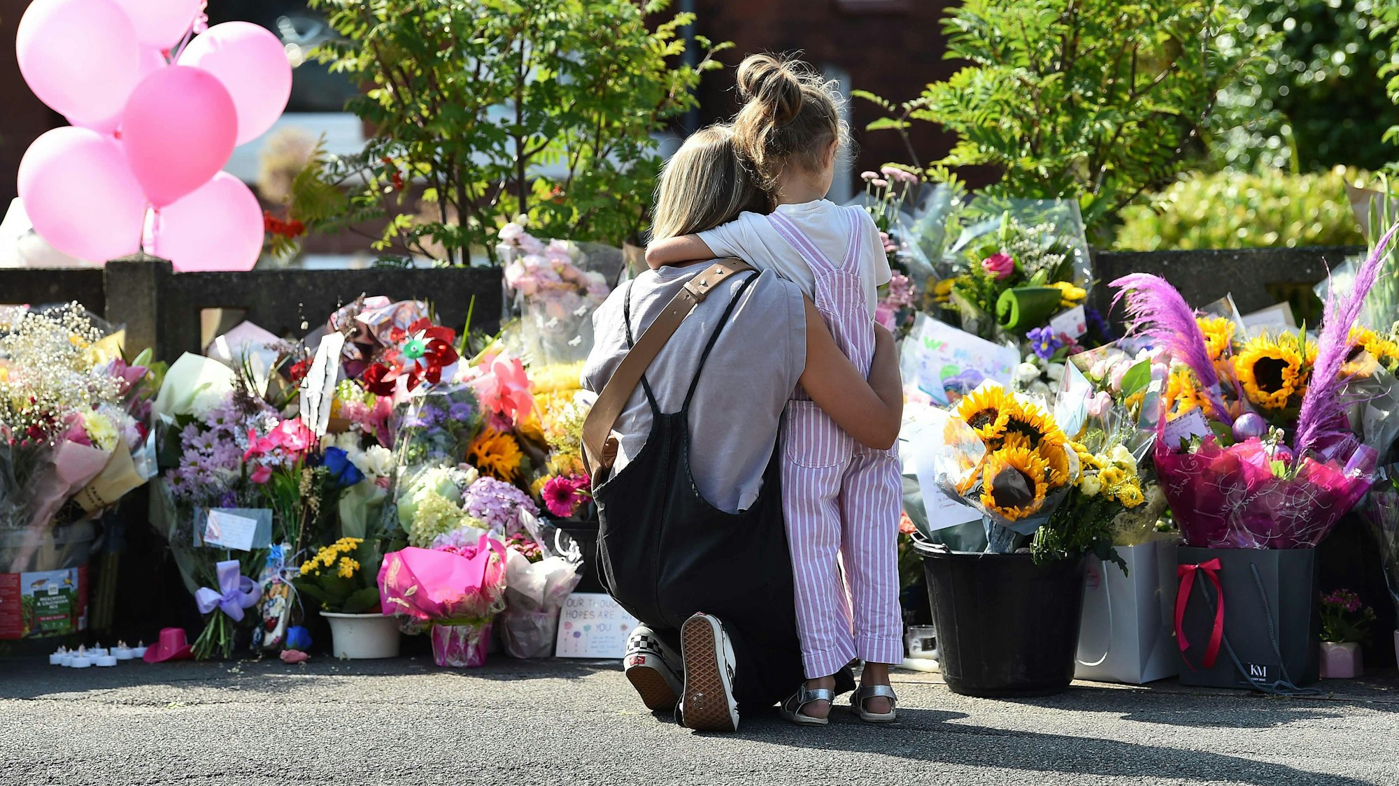 Eine Mutter umarmt ihr Kind vor einer Gedenkstelle für die Opfer des Messerangriffes auf tanzende Kinder in Southport.