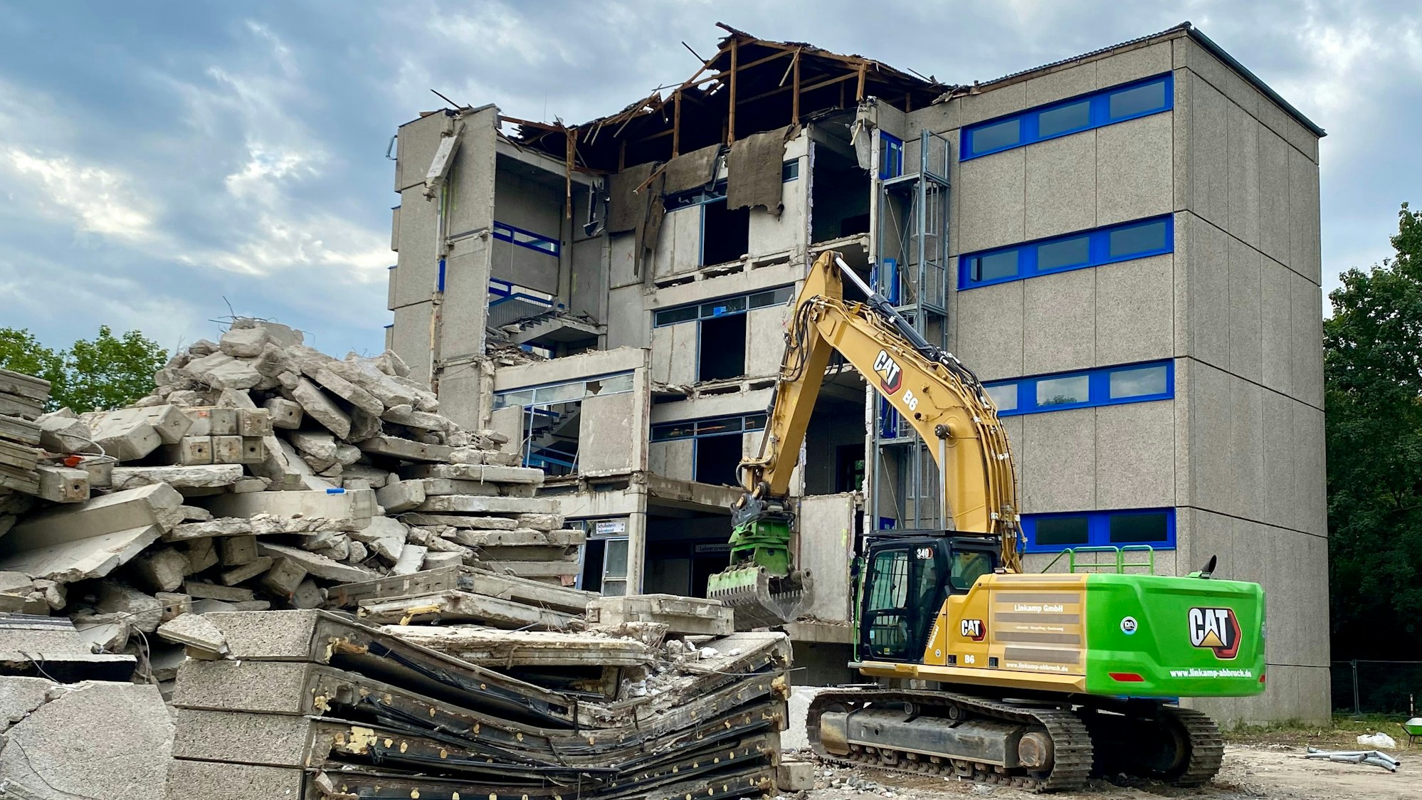 Das Bild zeigt einen Bagger vor dem zum Teil schon abgebrochenen Schulgebäude.
