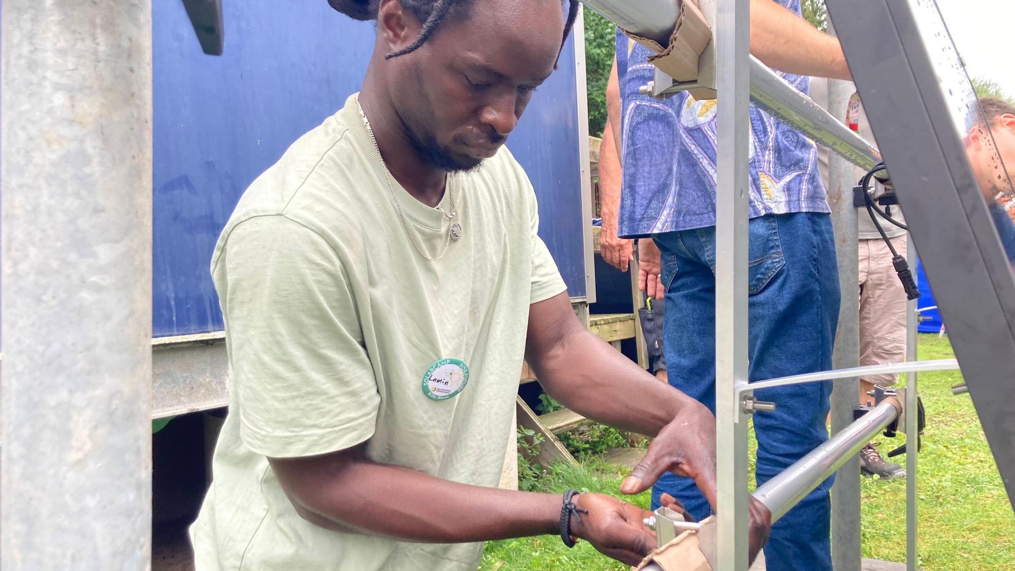 Camp-Teilnehmer Lamin Sey schraubt an einem Balkonsolar-Modul.