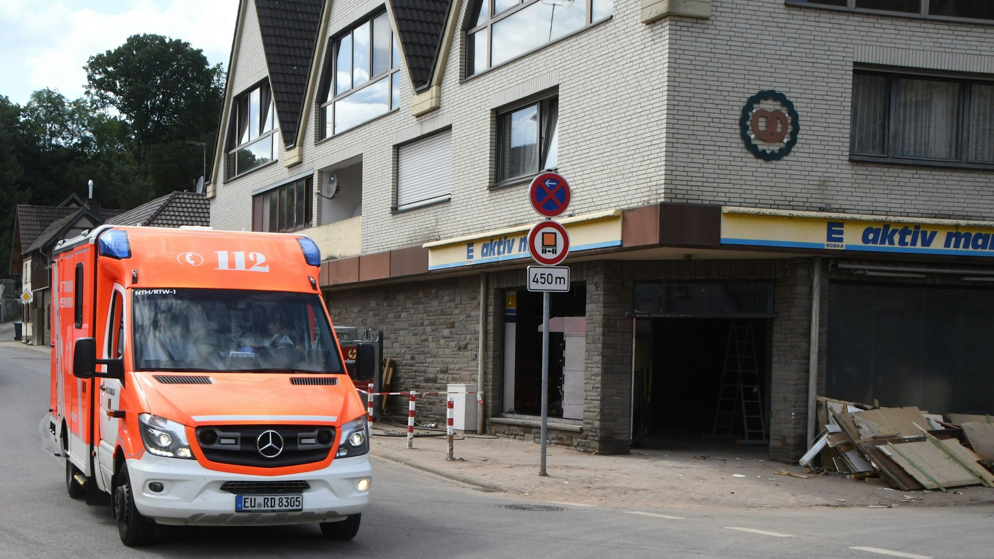 Schutt liegt vor dem kleinen Markt. Im Gebäude befand sich auch die Backstube. Ein Rettungswagen hält auf der Straße.
